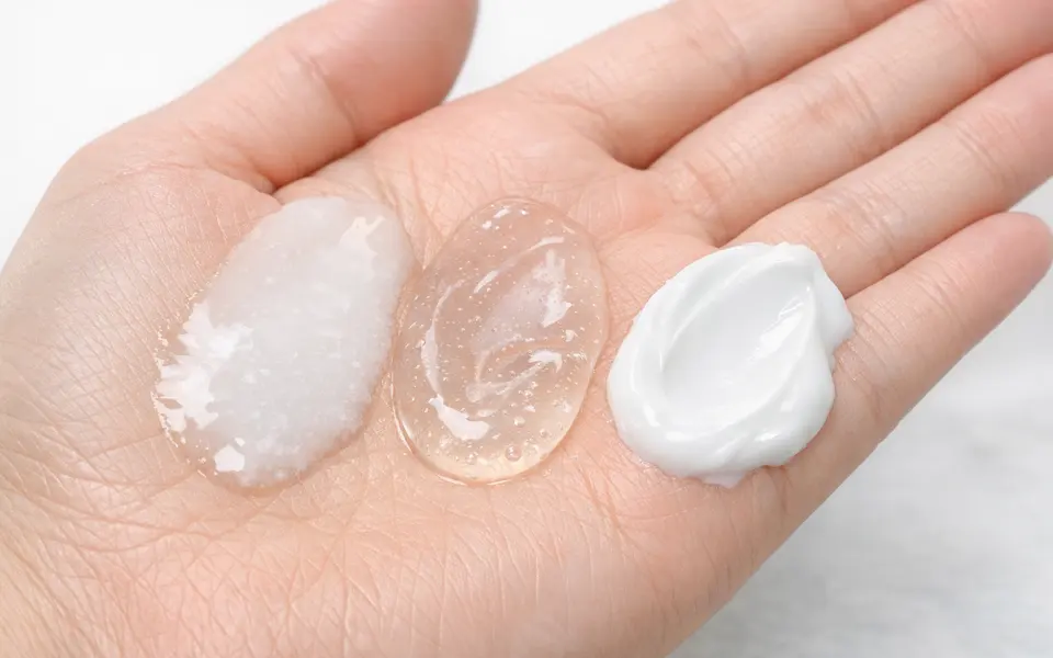 Close-up of different cleanser textures on a hand: gel, cream, and oil-to-milk, against a light background.
