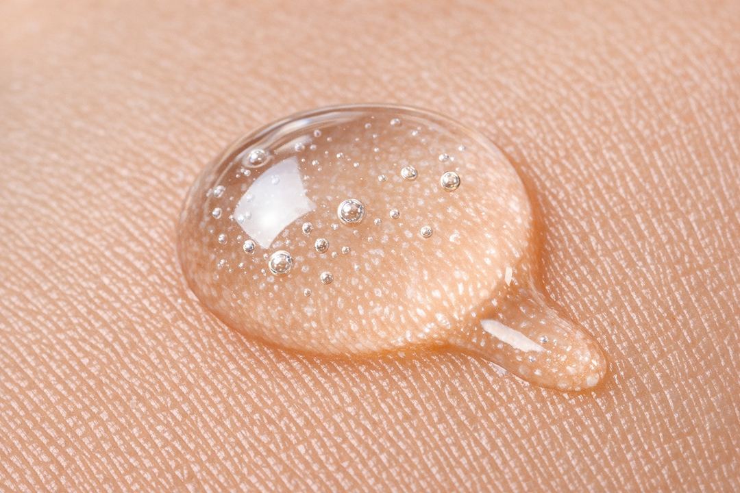 Close-up of a clear hyaluronic acid serum drop on skin to show texture